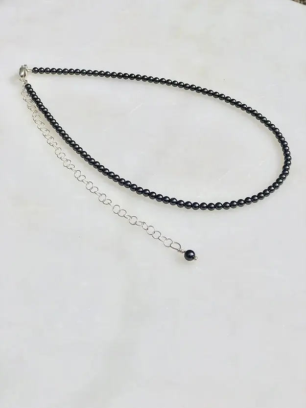 A 13-18” Black Pearl Necklace/Choker with a black bead and a silver chain.
