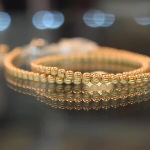 A 13-18" Bright Gold Pearl Choker/Necklace on a glass table.
