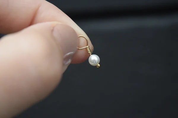 A person holding a White Pearl 4mm Dangle on a gold chain.