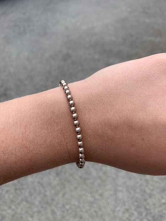A woman's hand holding a bronze pearl bracelet.