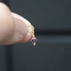 A person holding a small June Birthstone 4mm Dangle dangling from a gold earring.