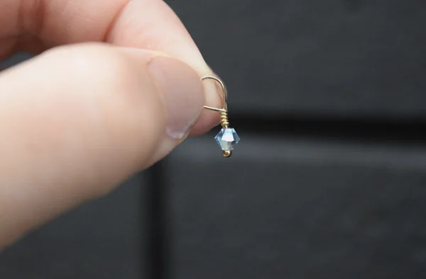 A person holding a March Birthstone 4mm Dangle dangling from a gold earring.
