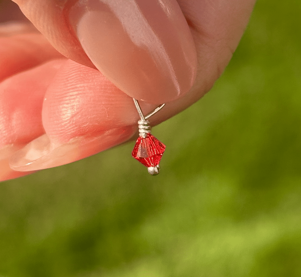 A person holding a small red July Birthstone 4mm Dangle.