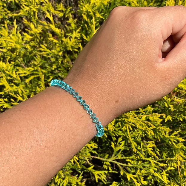A person wearing a December Birthstone - Turquoise Crystal Bracelet in front of bushes.