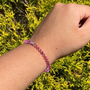 A person wearing an October Birthstone - Rose Crystal Bracelet in front of bushes.