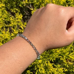A person's hand with a June Birthstone - Paradise Shine Crystal Bracelet in front of bushes.