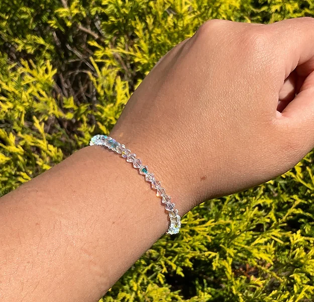 A person wearing an April Birthstone - Clear KIDS Crystal Bracelet in front of bushes.