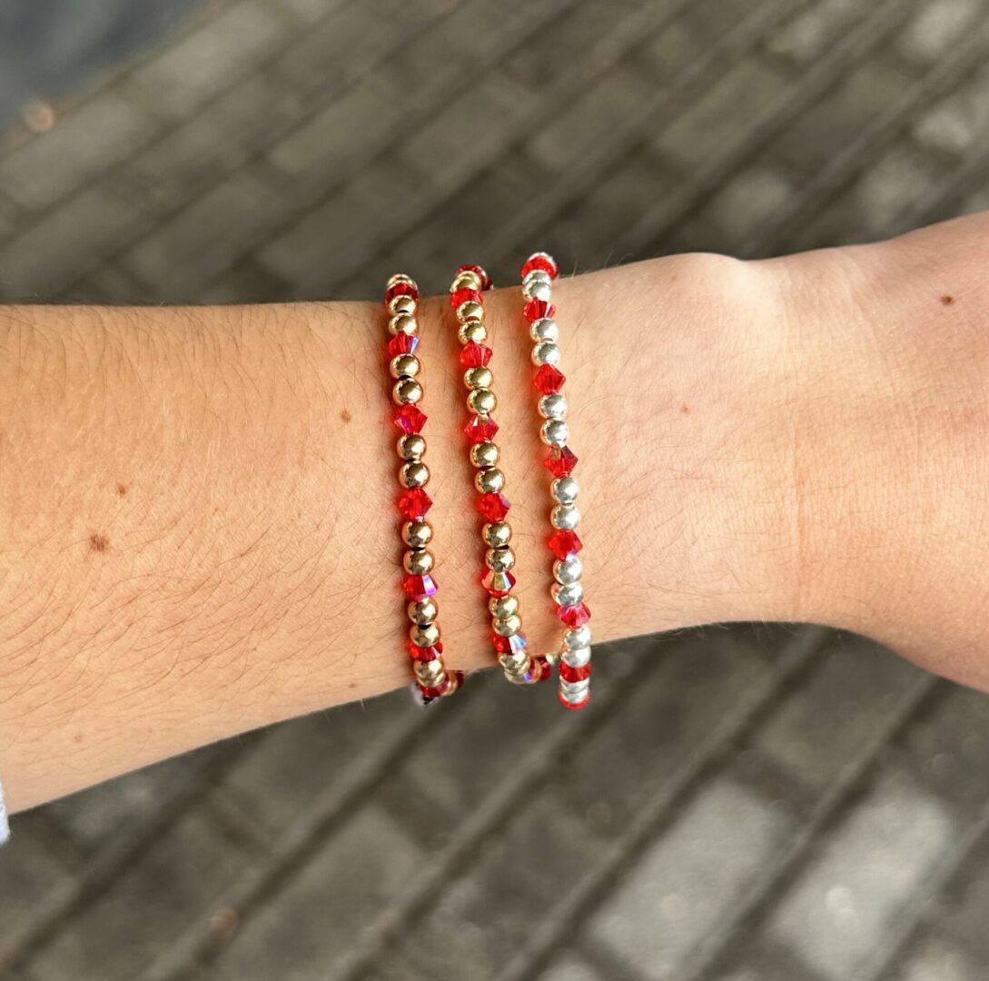 Three July Birthstone - Crystal Stretch Bracelets with red and silver beads on a woman's wrist.