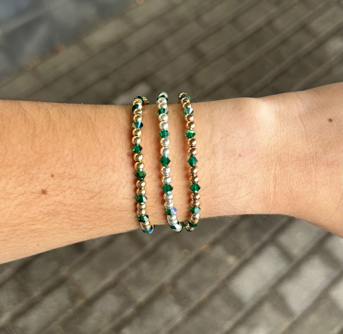 A woman's wrist with three May Birthstone - Emerald Crystal Stretch Bracelets on it.