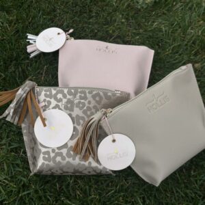 Three Hollis Chic Makeup Travel Bags with tags on them laying on the grass.
