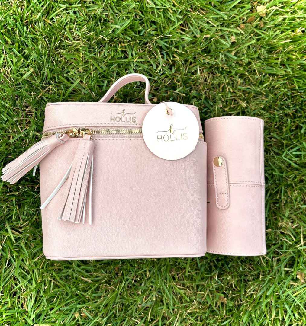 A Hollis Blush Mini Makeup Bag with Mini Brush Holder with a tassel sitting on the grass.