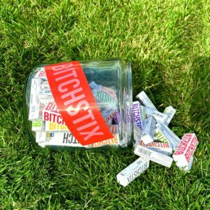 A BitchStix Lip Balms jar filled with candy on the grass.