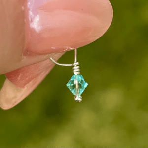 A person holding a small blue December Birthstone 4mm Dangle earring.