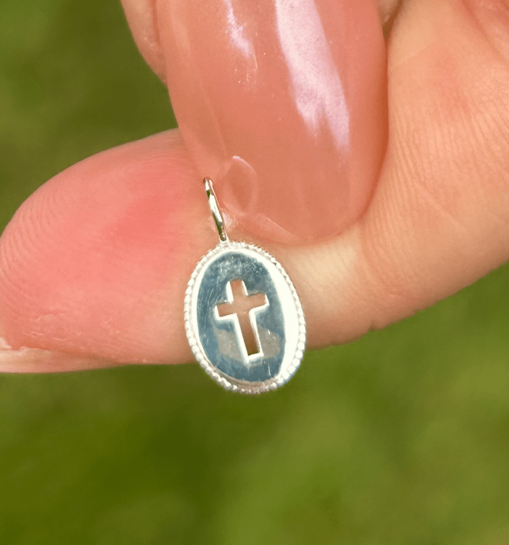 A person holding a small Sterling Silver Oval Cross Charm.