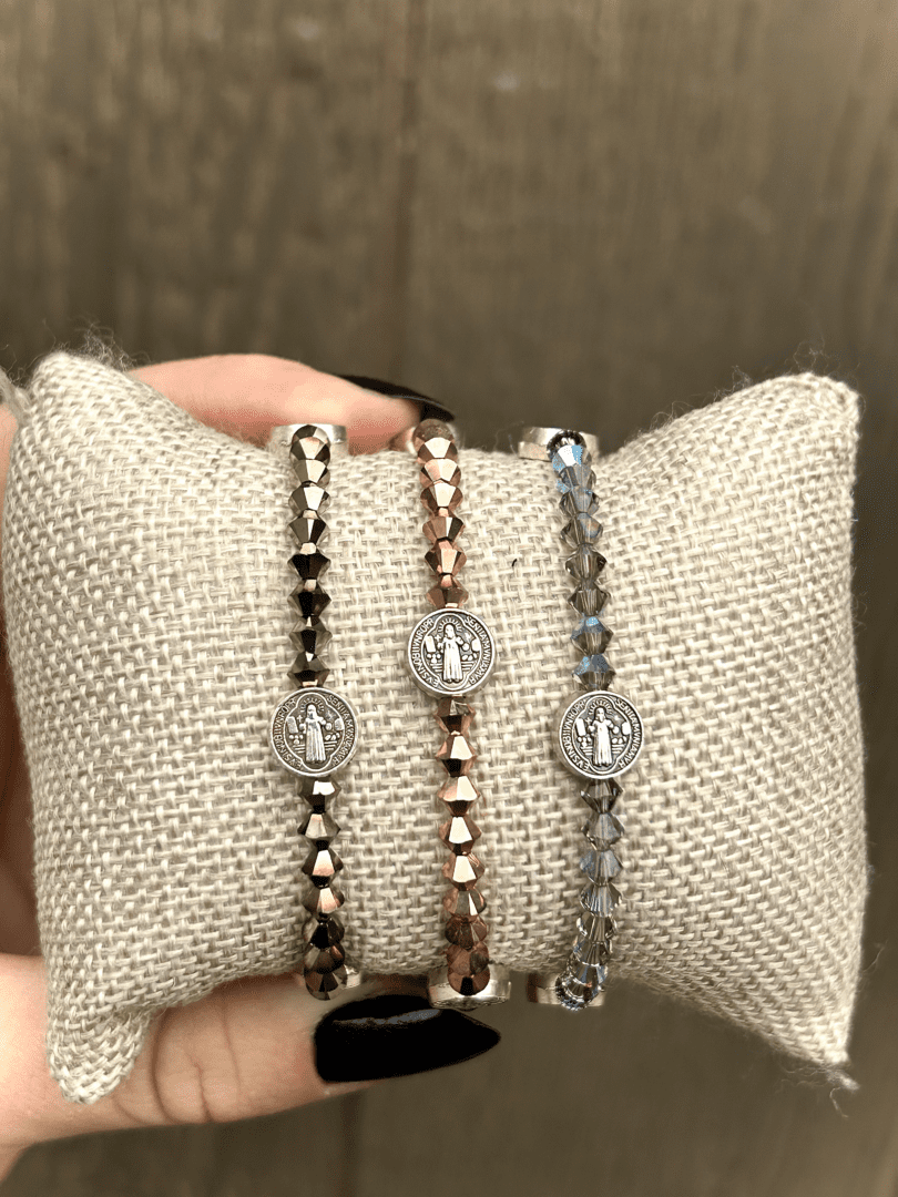 A person is holding three St. Benedict Bracelets on a pillow.